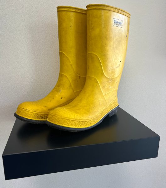 A used pair of yellow rain boots is displayed on a black shelf