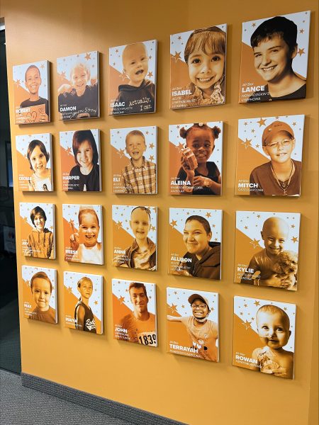 A mustard colored wall is decorated with 20 pictures of adorable smiling kids.