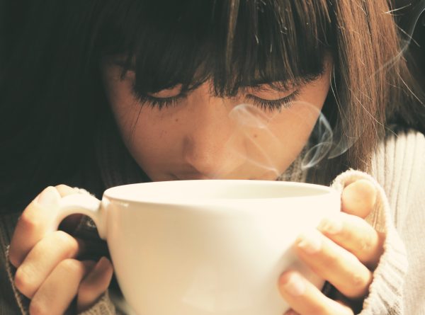 A person smelling a mug of steaming coffee