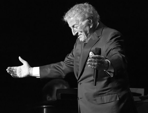 Black and white image of singer Tony Bennett bowing with a microphone
